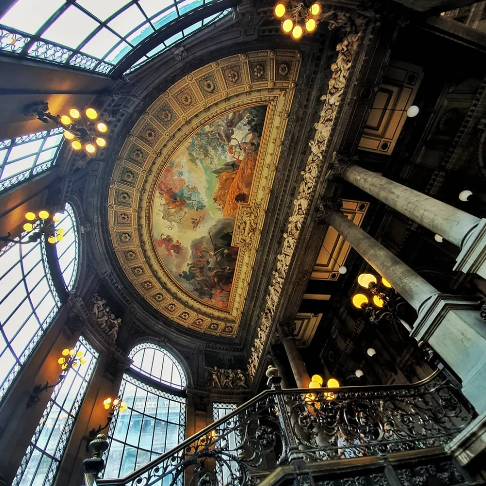 Looking up at an ornate ceiling with a painted dome and stained glass